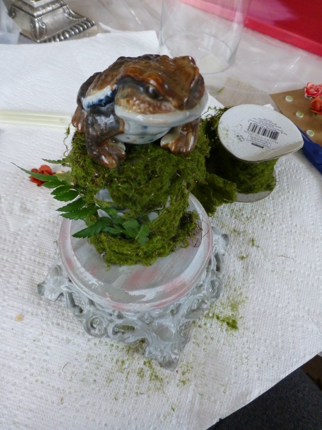 The toad gets glued onto the top of the moss-covered post, which is mounted to the wood base.