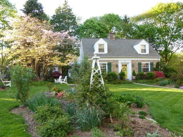 A photo of my little cottage taken last spring with one of my garden beds in the foreground.  This bed is positioned to be seen through the front windows of my house and enhances the view from the street as well.