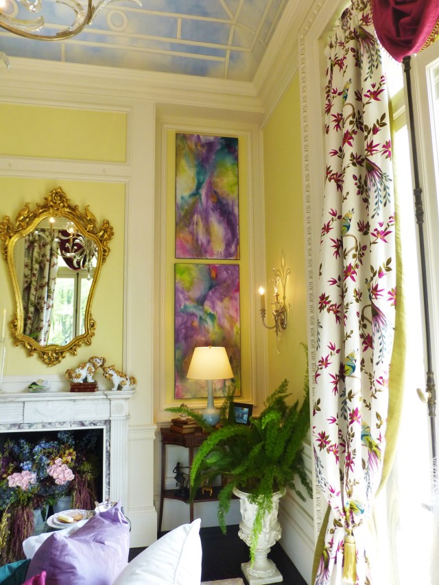 A small fireplace mantel has a shapely mirror placed above, and contemporary artwork enhances the corner.