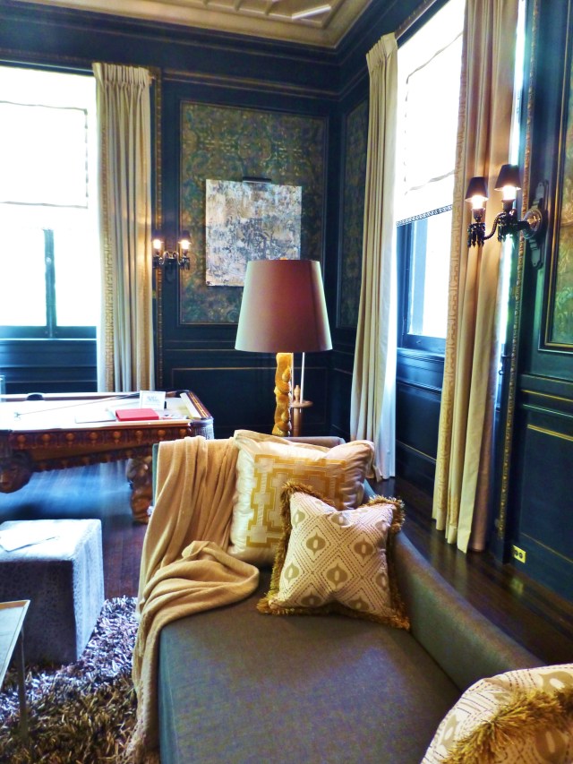 In this photo, you can appreciate how the light-colored draperies and pillows contrast beautifully with the dark walls. The designer chose to use gold accents, which enhance the gold leaf detailing of the paneling in the room. Notice the shaggy textured rug and brush fringe on the pillows--both of which update the space.