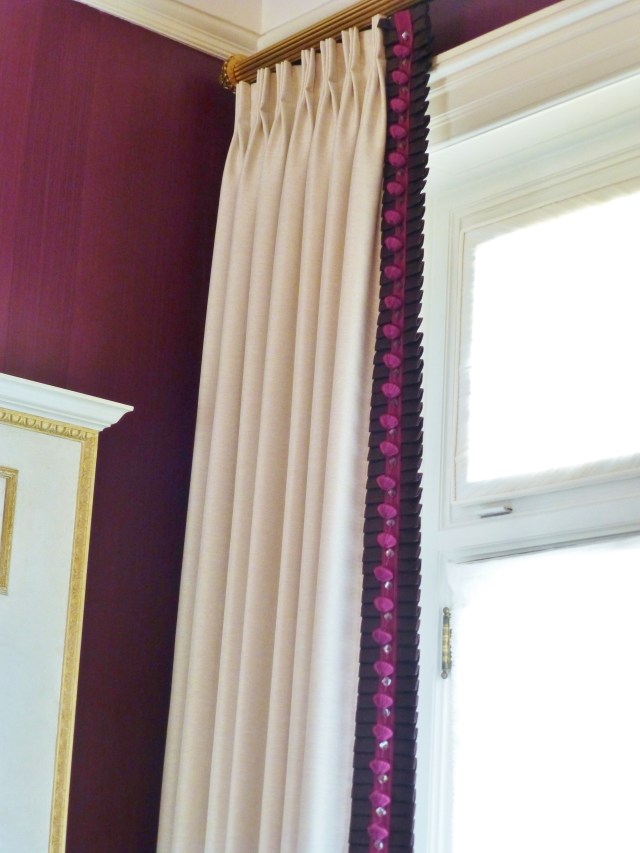 Solid white pleated draperies continue the play of contrasts with the dark walls.  These simple window treatments are treated to luxurious trim at the leading edge.