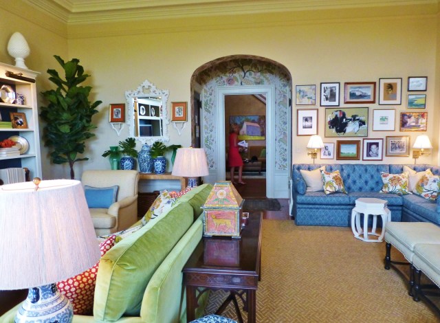 The entry alcove has wallpaper in the same pattern as the colorful pillows used throughout the room.  The designer did a great job of zoning the sitting areas in this space, with the main TV viewing area on the left and a custom banquette for lounging near the fireplace at the right.