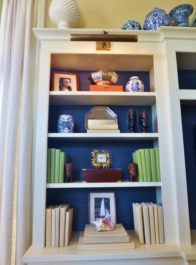 A detail of the cabinetry shows the artful arrangement of cherished objects.  The color-coordinated books are fabulous and the bold blue textured paper (grasscloth or possibly fabric?) looks terrific when placed in the back of the shelves.  Don't miss the beautiful library lights at the top of the shelves...I'm currently in the process of installing similar fixtures in my own home library!