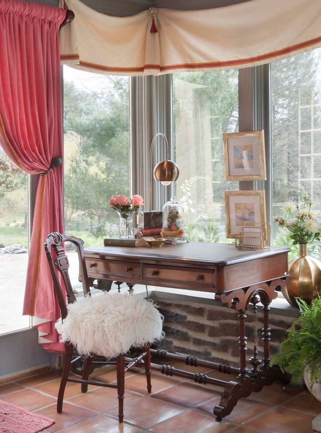 A handsome 19th century desk and chair are placed in the windows to allow for working while enjoying the view.  You can also see a close-up of the custom valances in this image.  The simple ivory linen-textured fabric is enhanced by a layered gold velvet and coral braid trim.  Starburst medallions and coral tassels are found at the junction of each soft swag. 