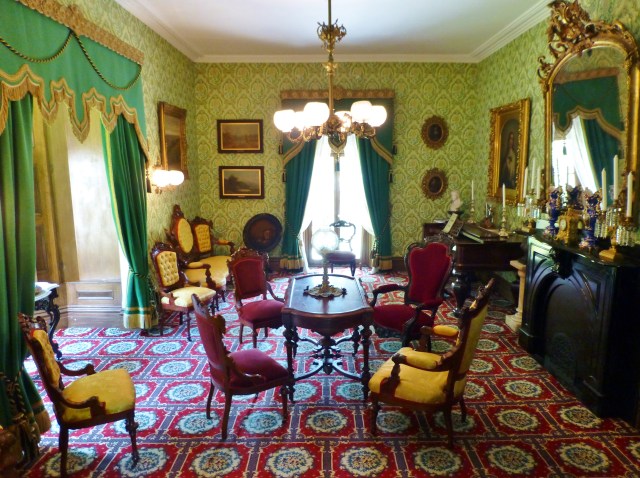 Wow, right?! The Victorians loved layering pattern.  This large floral geometric patterned wall-to-wall carpeting was a popular Victorian flooring choice in the second half of the nineteenth century.  The ornate bold green draperies feature gold bullion fringe and luxurious trimmings.  