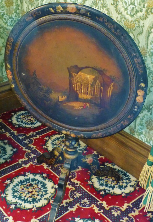 A detail of the charming hand-painted table.  The image is of a couple enjoying a Gothic ruin.  There are lovely flowers painted around the perimeter and on the legs.  