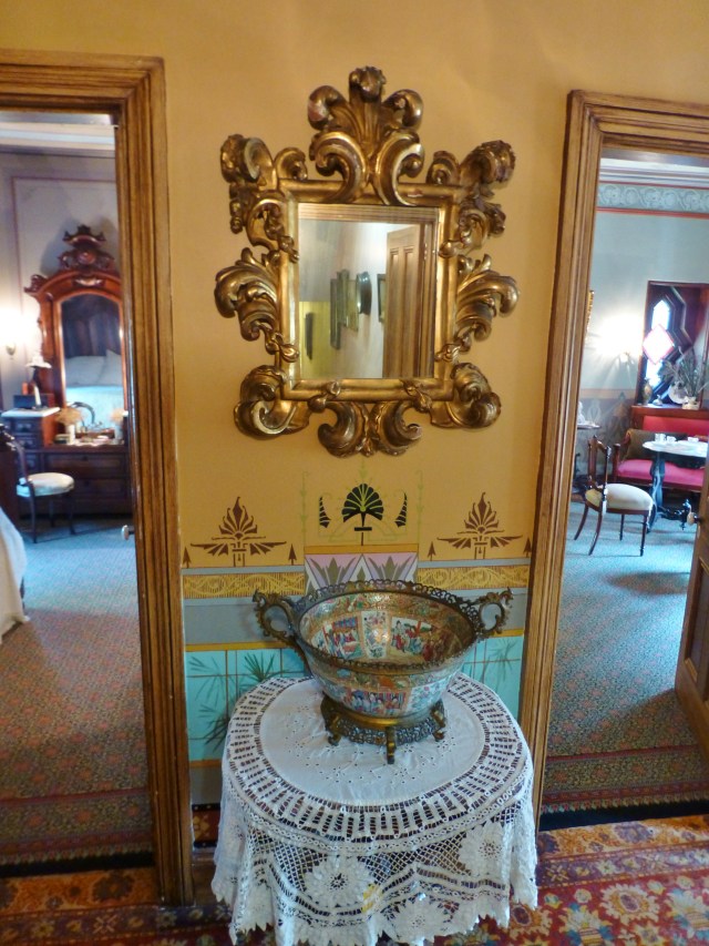 Back in the upstairs hallway, a stunning Italian-style gilded mirror welcomes you between the entrances of the two room suite.  From this vantage point (exiting the Children's room, behind you) the bedroom is at the left and the lounge at the right.  Notice the handpainted wainscoting behind the lace-covered table.  You'll also notice the layering of patterns with the area rugs in this image.  