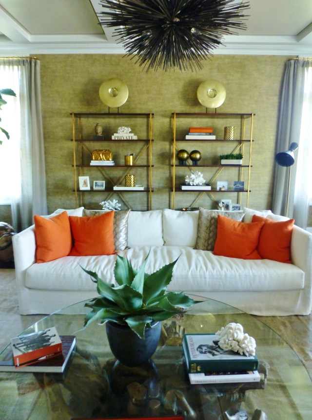 The living room has entrances from either side of the great room fireplace.  This image is your first impression upon entering the room.   The pair of gold metallic etageres are beautifully arranged and the large comfortable sofa has bold pillows that inject the bold orange accent color into the room's design.
