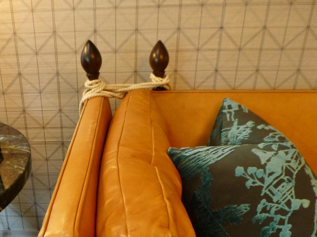 A detail of the Knole sofa.  It features adjustable side arms and considerable depth of seating, it usually has exposed wooden finials at the rear corner tops, and some exposed wood may be present on the otherwise arms. The arms, more correctly sides, are of the same height. The side arms are tied to the sofa back by means of heavy decorative braid, often with an elaborate tassel.