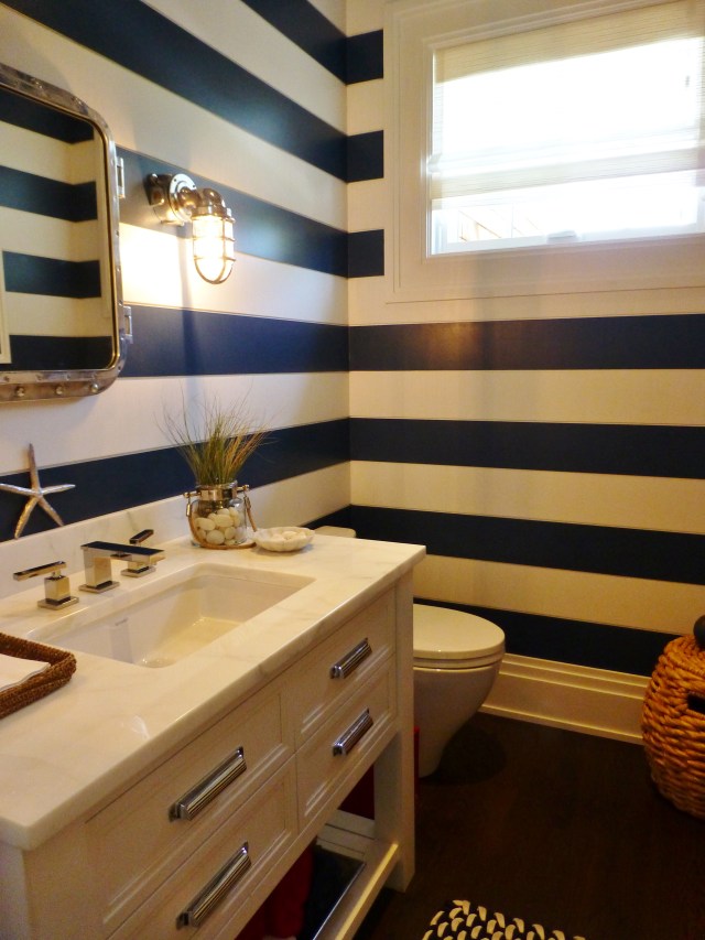 The adjoining powder room is also clad in ship-lap siding, painted in alternating stripes.  This contributes to the updated nautical theme, along with the ship lights and riveted metal framed mirror.  The rope basket in the corner gives some texture and warmth too.  This is a terrific powder room!