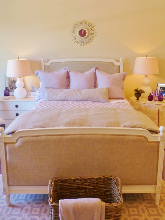 The French linen-upholstered bed is topped by lovely lavendar bedding.  The pair of white glass gourd lamps are quite pretty, as is the ivory starburst mirror above the bed.