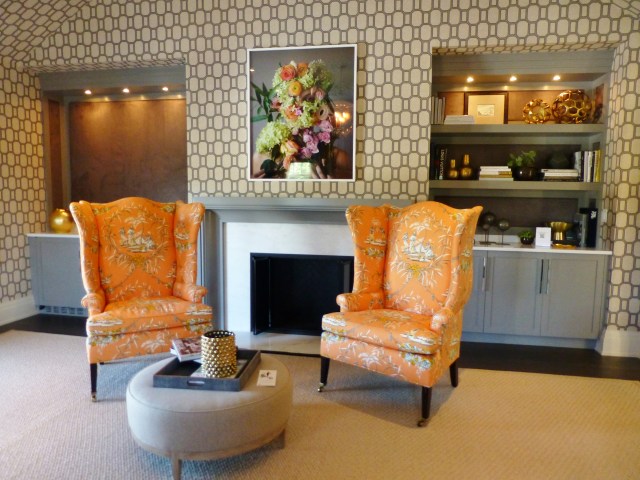 Directly across from the foot of the bed is a lovely seating area and fireplace.  There are even built in bookshelves at the right and a wet-bar at the left!   The curvy wing-back chairs are covered in the same orange toile, and a round grey ottoman is used as a cocktail (or coffee if you prefer) table. The colorful artwork above the mantel is truly amazing.  At first glance it just looks like a photograph of flowers, but upon closer inspection, once notices an eye peeking out from the foliage and then naked shoulders with fingers clutching the bouquet the bottom of the image.  I love art that takes a few minutes to reveal itself!