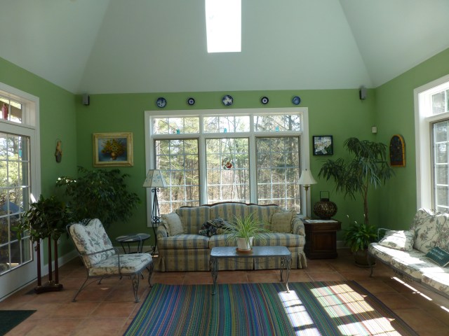 BEFORE:  Bold green on the walls and a soft turquoise on the tray ceiling are vibrant and exciting in this conservatory, but the vintage iron furniture is leggy and small, while the striped rug is undersized and not relevant to the furniture placement.   