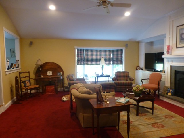 In this photograph you can see the lovely high angled ceilings in the large space.  The furniture placement felt a little jumbled, however, and the red carpet really needed to go!   The inside-mounted window treatments didn't enhance the large bay window at all. Plaid roman shades visually brought the window down and made the whole thing feel very heavy. 