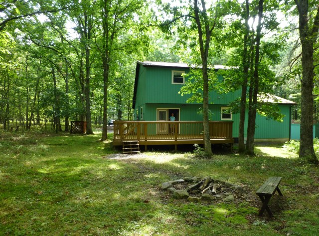 The back side of The Shack, shows the large back deck, the rudimentary fire pit, and the lovely bit of woods upon which the house is located. 